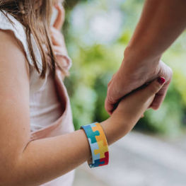 Image showing a adult holding a child's hand. The child is wearing an autism awareness bracelet.